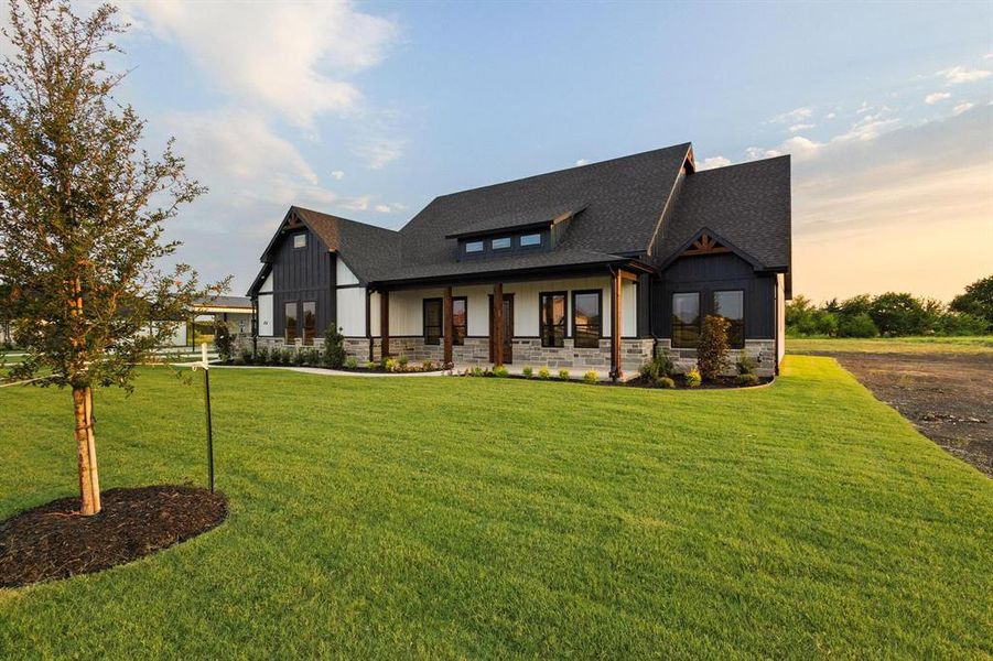 View of front of property with stone siding, covered porch, a front lawn, and board and batten siding