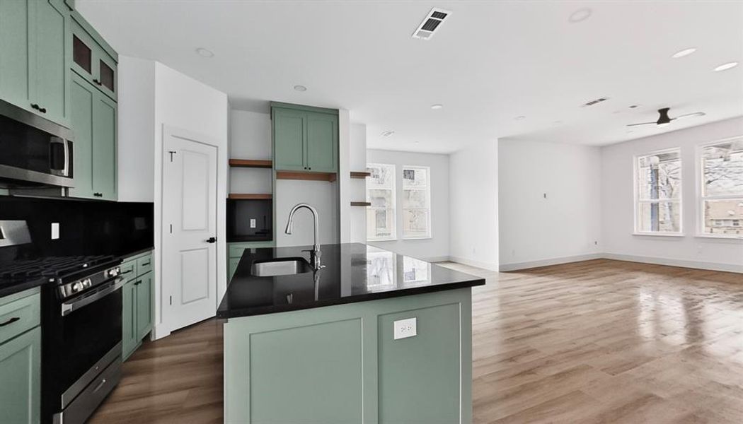 Dual tone kitchen featuring stainless steel appliances, a kitchen island with sink, dark stone countertops, dark wood-style flooring, and dual tone cabinetry