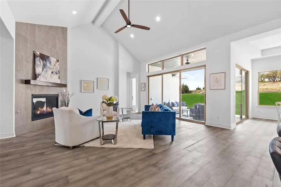 Living room featuring a ceiling fan, beam ceiling, high vaulted ceiling, a fireplace, and wood finished floors