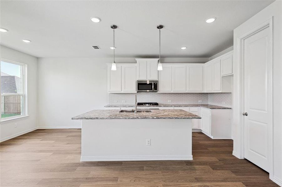 Kitchen featuring decorative backsplash, wood-type flooring, light stone counters, and white cabinets