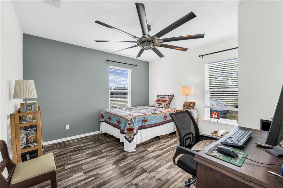 Bedroom with multiple windows, dark wood-style floors, a ceiling fan, and an office area
