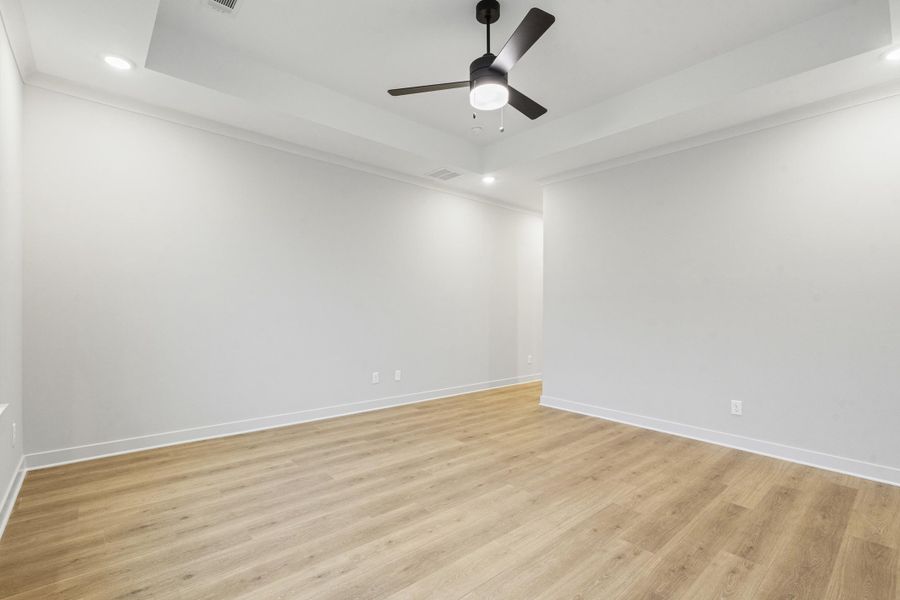 Spacious room featuring wood-finish flooring, a tray ceiling, recessed lighting, and a contemporary ceiling fan Spacious room featuring wood-finish flooring, a tray ceiling, recessed lighting, and a contemporary ceiling fan