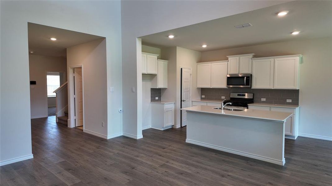 Kitchen with dark wood finished floors, backsplash, light countertops, stainless steel appliances, and recessed lighting