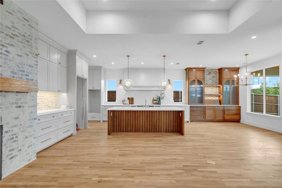 Kitchen featuring suspended lighting, a kitchen island with sink, light wood finished floors, backsplash, and dual tone cabinetry