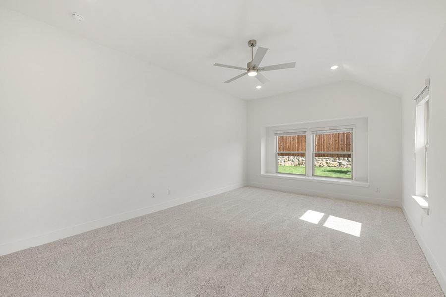 Empty bedroom with vaulted ceiling, ceiling fan, carpet flooring, and backyard-facing window Empty bedroom with vaulted ceiling, ceiling fan, carpet flooring, and backyard-facing window