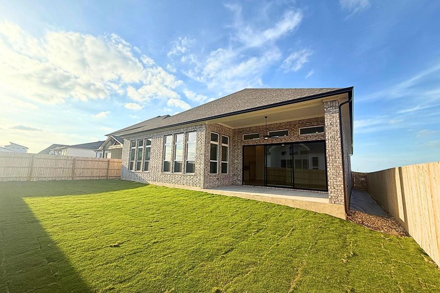 Rear exterior featuring a covered patio with pendant lighting, three-panel sliding glass doors, multiple large windows, and a brick façade
