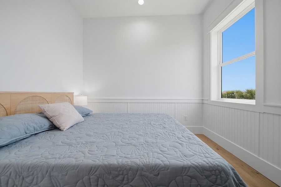 Bright bedroom with a cozy bed, elegant wainscoting, and a large window offering plenty of natural light and a serene view.