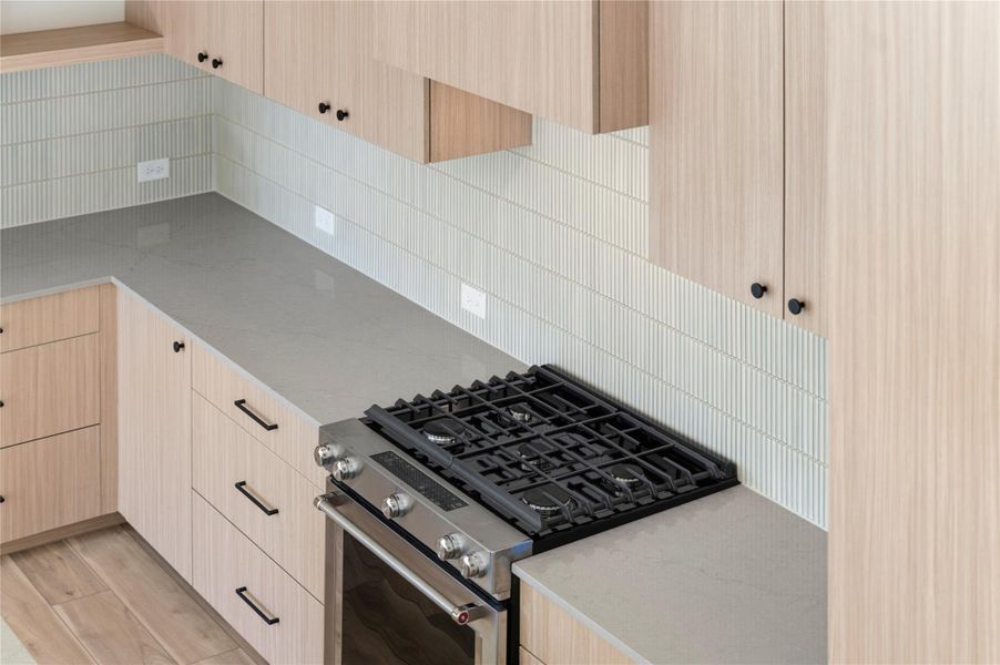 Kitchen featuring light brown cabinets, stainless steel range with gas cooktop, light stone counters, backsplash, and modern cabinets Kitchen featuring light brown cabinets, stainless steel range with gas cooktop, light stone counters, backsplash, and modern cabinets