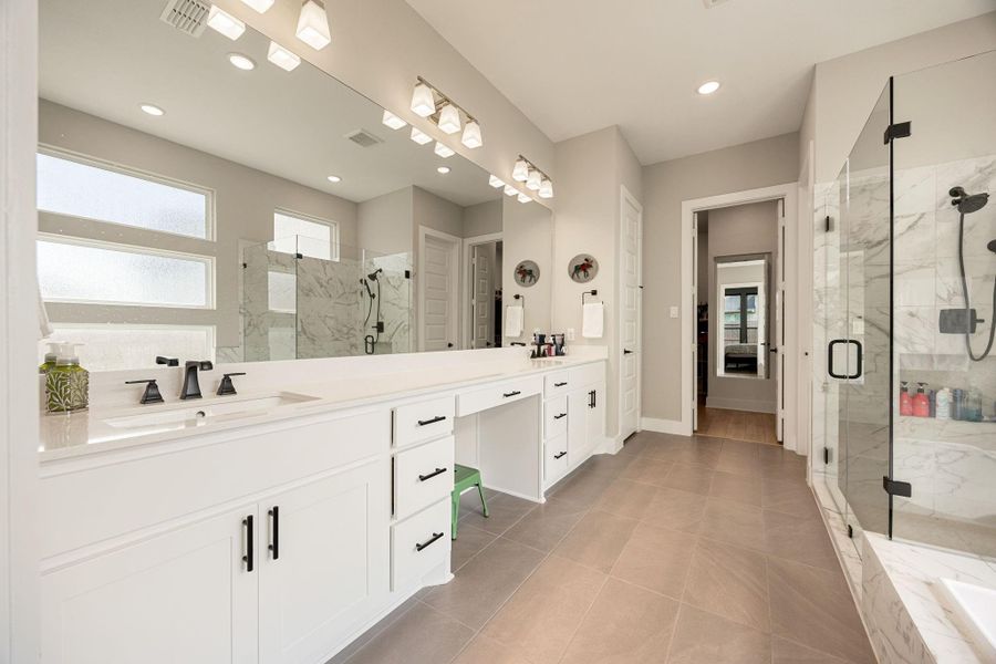 This luxurious primary bathroom showcases an expansive double vanity with sleek quartz countertops and ample storage. A frameless glass-enclosed shower with elegant marble tile pairs perfectly with the soaking tub for a spa-like experience. Modern fixtures, designer lighting, and neutral finishes create a bright, sophisticated retreat.