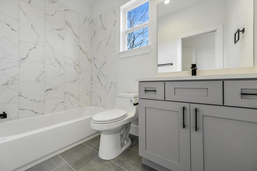 Clean, crisp, and sophisticated. The floor-to-ceiling marble-patterned tile creates a spa-like retreat, perfectly balanced by a modern grey vanity and sleek matte black hardware.