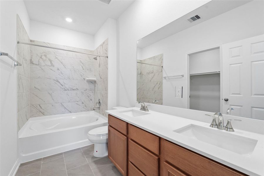This beautifully updated primary bathroom is move-in ready! It showcases stained cabinetry paired with light countertops, dual vanity sinks, a large mirror, spacious walk-in closet with built-in shelving, high ceilings, custom paint, and stylish modern finishes throughout.