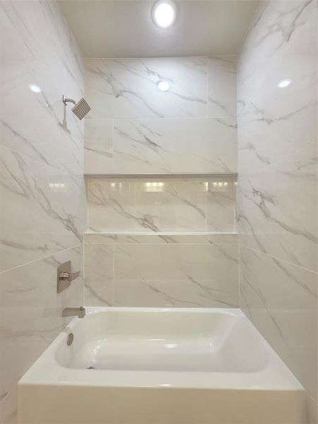 Hallway bathroom with custom tile and bathtub, with niche for shampoos.