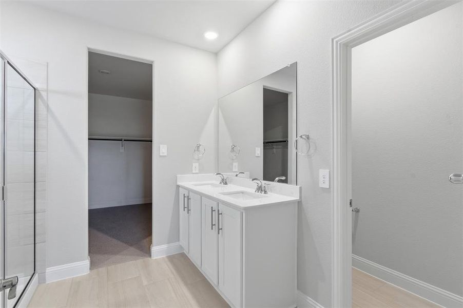 Bathroom featuring a dual vanity with white cabinetry and a large mirror, a glass-enclosed shower, and light-colored flooring