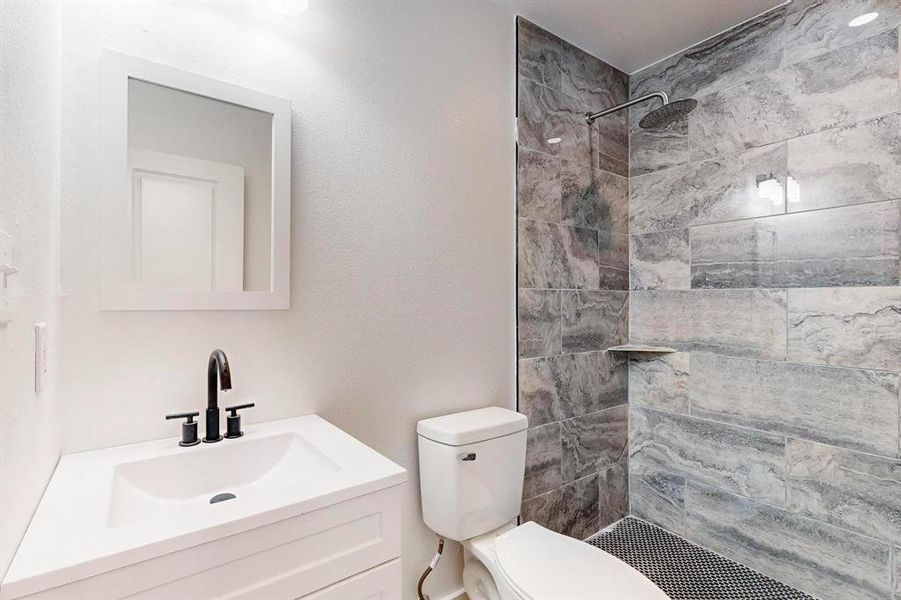 Bathroom with tiled shower, vanity, and toilet