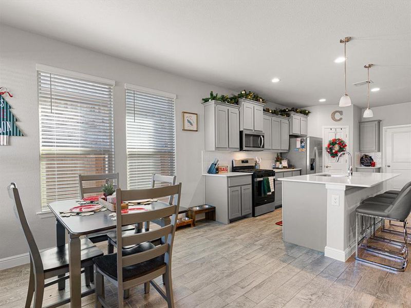 Kitchen with a center island with sink, gray cabinets, appliances with stainless steel finishes, decorative light fixtures, and light hardwood / wood-style floors