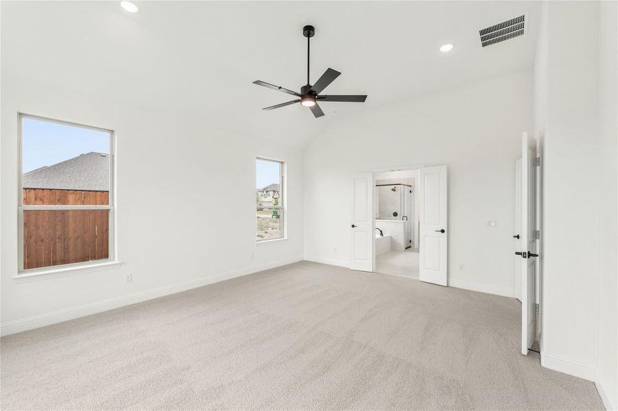 Spacious master bedroom with vaulted ceiling, black ceiling fan, carpet flooring, and open ensuite bathroom doorway. Spacious master bedroom with vaulted ceiling, black ceiling fan, carpet flooring, and open ensuite bathroom doorway.
