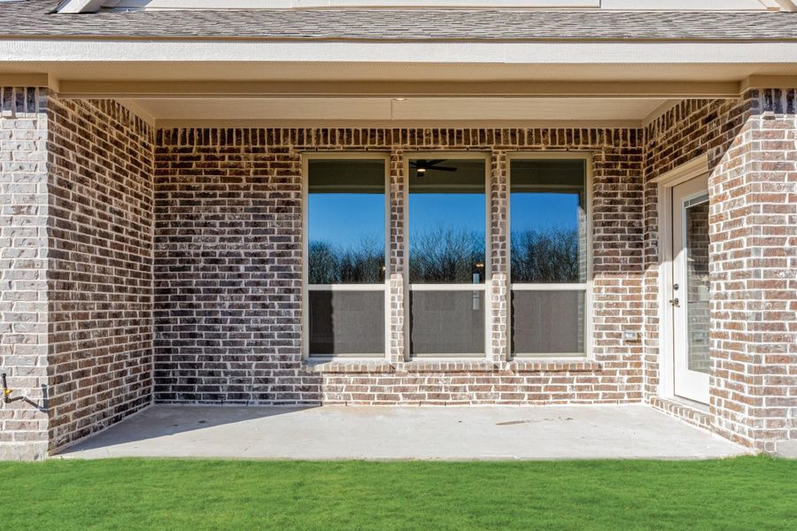 Covered back patio with brick exterior, large windows, and concrete slab overlooking green lawn