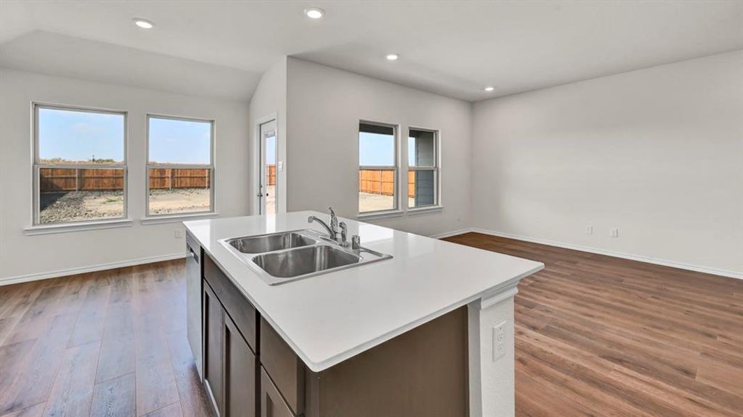 Kitchen island featuring a double basin stainless steel sink with a chrome faucet, white countertop, and dark wood-finish cabinetry