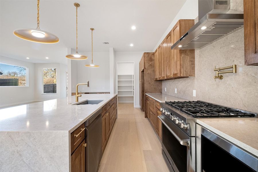 Kitchen featuring light stone countertops, stainless steel appliances, backsplash, light wood-type flooring, and decorative light fixtures