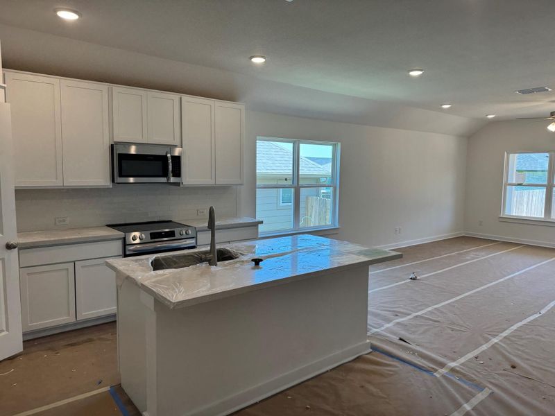 Kitchen with stainless steel appliances, lofted ceiling, white cabinetry, decorative backsplash, and open floor plan Kitchen with stainless steel appliances, lofted ceiling, white cabinetry, decorative backsplash, and open floor plan