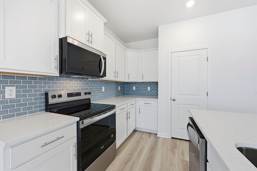 Kitchen with stainless steel appliances, white cabinets, light stone countertops, light wood-style floors, and recessed lighting Kitchen with stainless steel appliances, white cabinets, light stone countertops, light wood-style floors, and recessed lighting