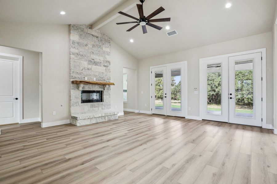 Unfurnished living room with beamed ceiling, light wood-style floors, a fireplace, a ceiling fan, and french doors