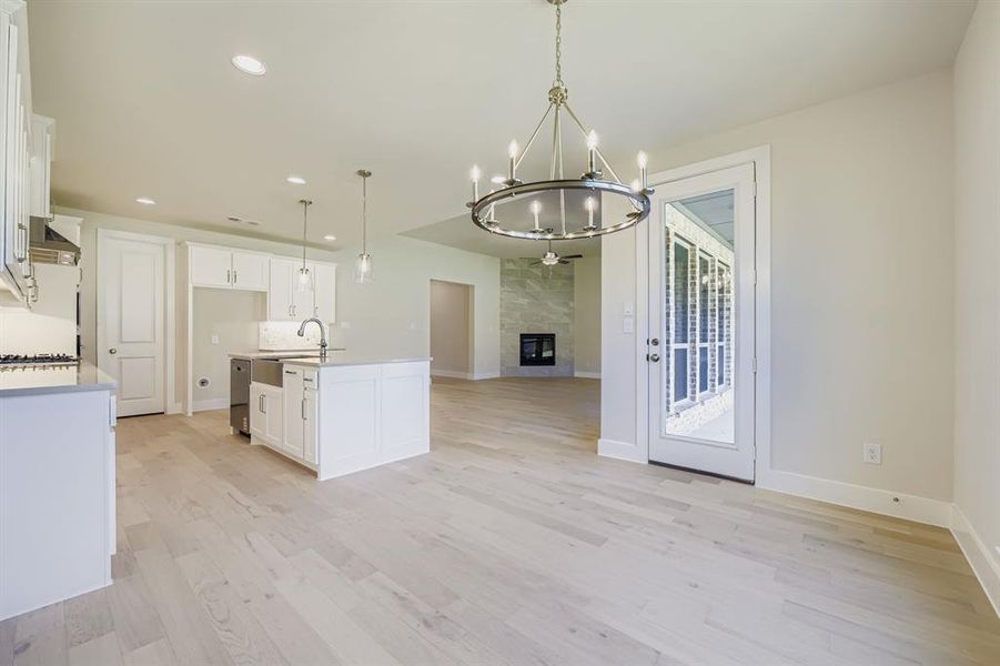 Kitchen featuring recessed lighting, a center island with sink, decorative light fixtures, light wood-style floors, and white cabinetry
