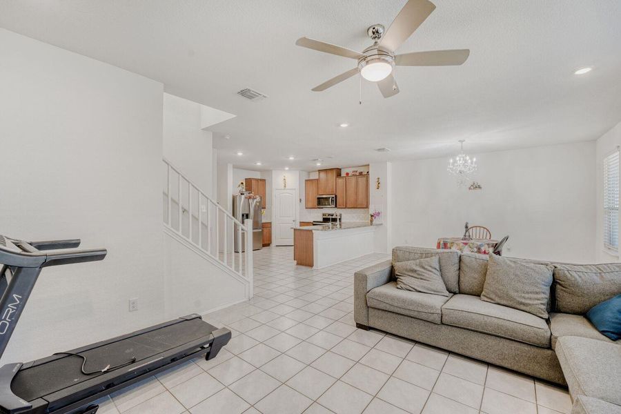 Living area with stairway, a ceiling fan, light tile patterned floors, recessed lighting, and a chandelier