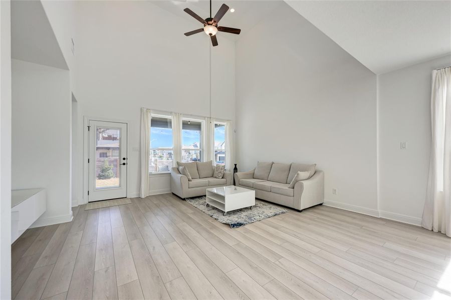 Vaulted ceilings with a ceiling fan, light wood-finish flooring, and multiple windows with sheer drapery