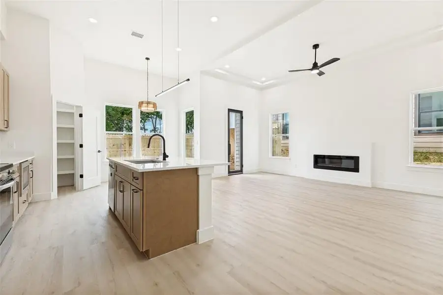 Spacious open-concept living area featuring light wood-finish flooring, a contemporary linear fireplace, and a tray ceiling Spacious open-concept living area featuring light wood-finish flooring, a contemporary linear fireplace, and a tray ceiling