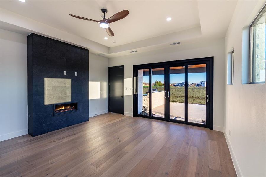 Empty room with a tile fireplace, hardwood / wood-style flooring, ceiling fan, a tray ceiling, and french doors