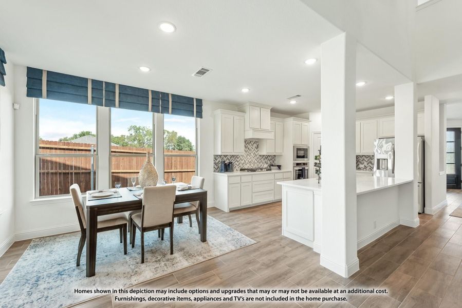 Open-plan dining area and kitchen with white cabinets, island, wood-look floors, and large windows with blue valances. Open-plan dining area and kitchen with white cabinets, island, wood-look floors, and large windows with blue valances.