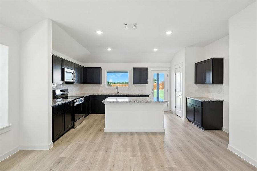 Kitchen with stainless steel appliances, lofted ceiling, decorative backsplash, dark cabinets, and light stone counters Kitchen with stainless steel appliances, lofted ceiling, decorative backsplash, dark cabinets, and light stone counters