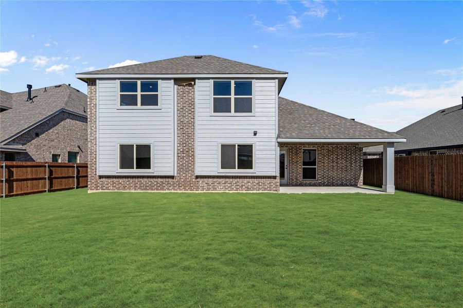 Two-story home rear view with brick and white siding, covered patio, and large fenced backyard
