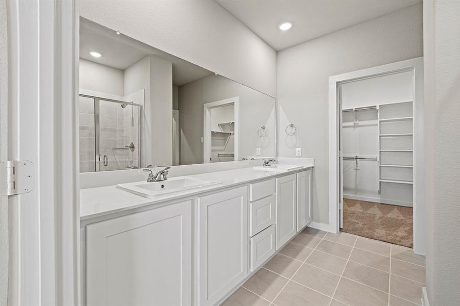 Bathroom featuring a shower with door, double sink, vanity with extensive cabinet space, and tile flooring