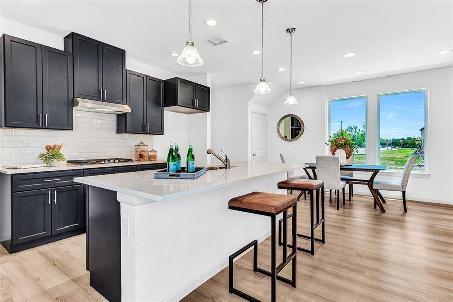 Kitchen featuring tasteful backsplash, light hardwood / wood-style flooring, hanging light fixtures, and a center island with sink