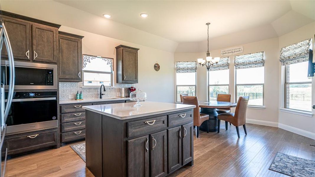 Gourmet kitchen featuring wood-finish flooring, dark wood cabinetry, a central island with a light-colored countertop, and a built-in oven and microwave