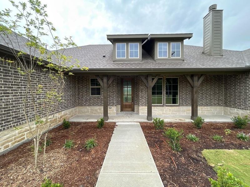 Front exterior featuring dark brick and light stone veneer, a covered porch with exposed timber posts, and a wood-finish entry door Front exterior featuring dark brick and light stone veneer, a covered porch with exposed timber posts, and a wood-finish entry door