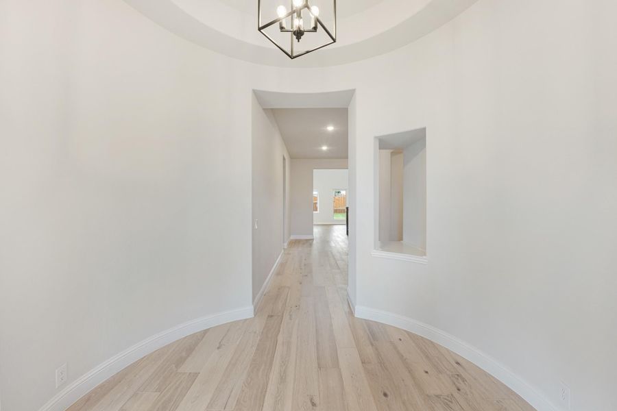Rounded entryway with tray ceiling, black chandelier, light hardwood floors, and hallway leading to main living area Rounded entryway with tray ceiling, black chandelier, light hardwood floors, and hallway leading to main living area