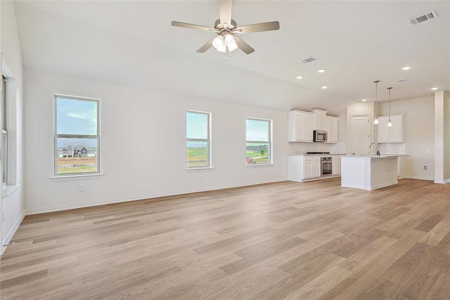 Unfurnished living room with light hardwood / wood-style flooring, vaulted ceiling, ceiling fan, and sink