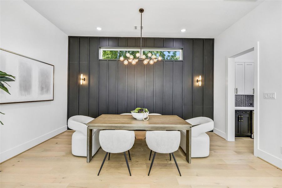 Elegant dining area featuring a dramatic charcoal accent wall with vertical millwork detailing and a statement modern chandelier. The transom window adds soft natural light while maintaining privacy. Clean lines, warm white oak flooring, and layered lighting create a refined space perfect for intimate gatherings or formal entertaining. Elegant dining area featuring a dramatic charcoal accent wall with vertical millwork detailing and a statement modern chandelier. The transom window adds soft natural light while maintaining privacy. Clean lines, warm white oak flooring, and layered lighting create a refined space perfect for intimate gatherings or formal entertaining.