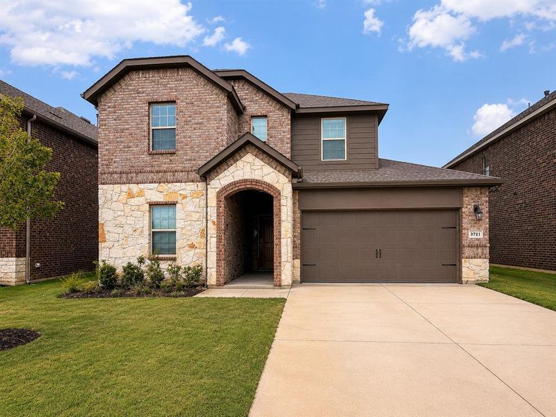 Brick and stone facade featuring an arched entryway, attached garage with carriage-style doors, concrete driveway, and established front lawn with landscaping Brick and stone facade featuring an arched entryway, attached garage with carriage-style doors, concrete driveway, and established front lawn with landscaping