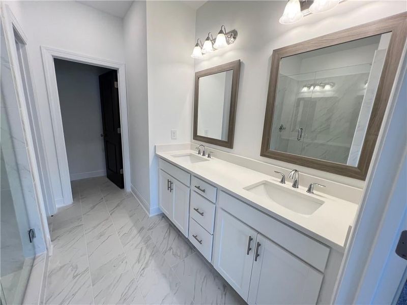 Owners Bathroom featuring double vanity, a stall shower, and marble finish flooring