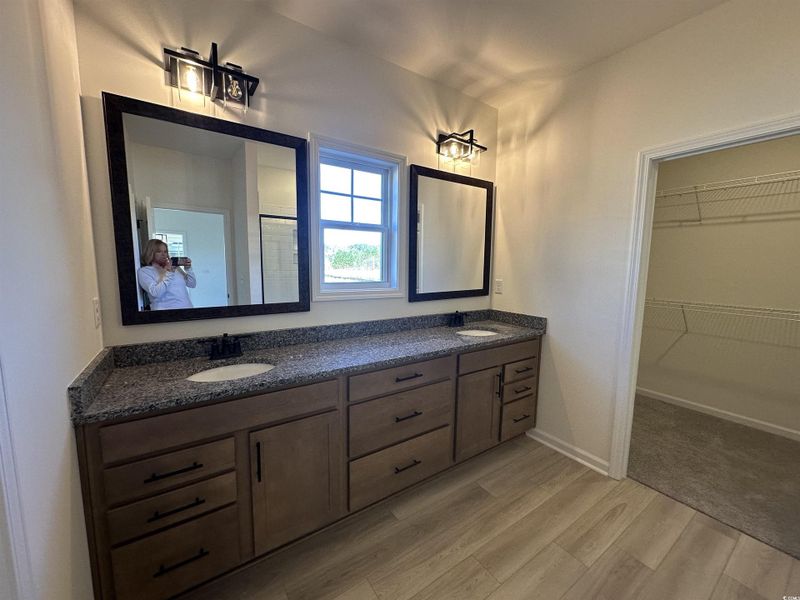 Bathroom with double vanity, a spacious closet, light wood-style flooring, and an enclosed shower