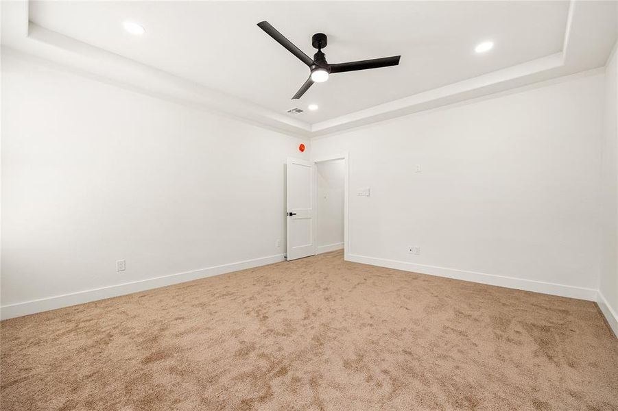 This photo showcases a spacious, freshly painted room with neutral walls and carpet flooring. It features recessed lighting, a modern ceiling fan, and a clean, minimalist design, perfect for a bedroom or office space.