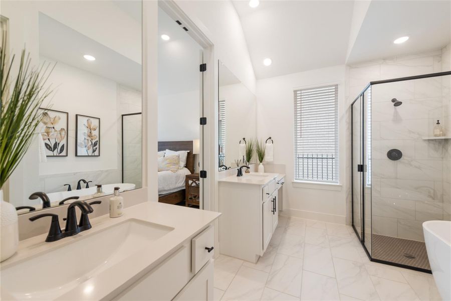A bright bathroom with twin vanities and a modern glass shower adjoins a serene bedroom. A bright bathroom with twin vanities and a modern glass shower adjoins a serene bedroom.