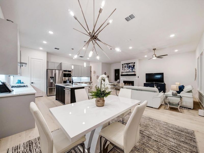 Dining space with a chandelier, light wood-style floors, a warm lit fireplace, recessed lighting, and a ceiling fan Dining space with a chandelier, light wood-style floors, a warm lit fireplace, recessed lighting, and a ceiling fan