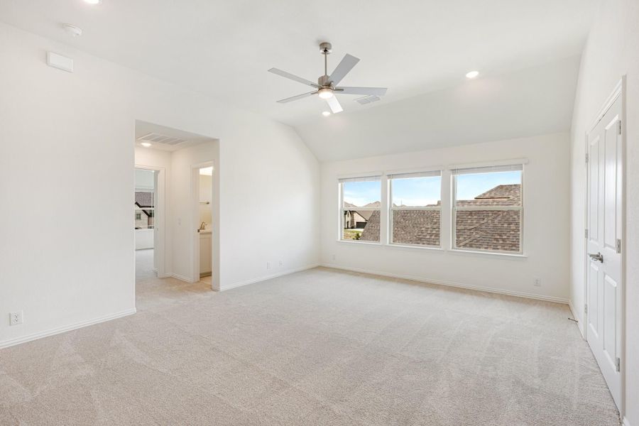 Spacious bedroom with vaulted ceiling, ceiling fan, carpet flooring, and ensuite bathroom doorway Spacious bedroom with vaulted ceiling, ceiling fan, carpet flooring, and ensuite bathroom doorway