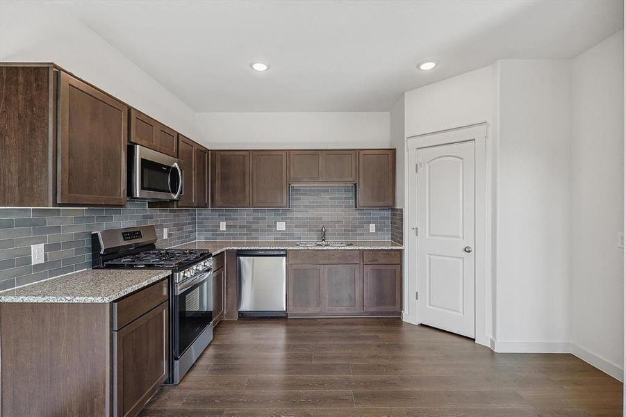 Kitchen featuring stainless steel appliances, sink, dark brown cabinets, dark hardwood / wood-style floors, and decorative backsplash