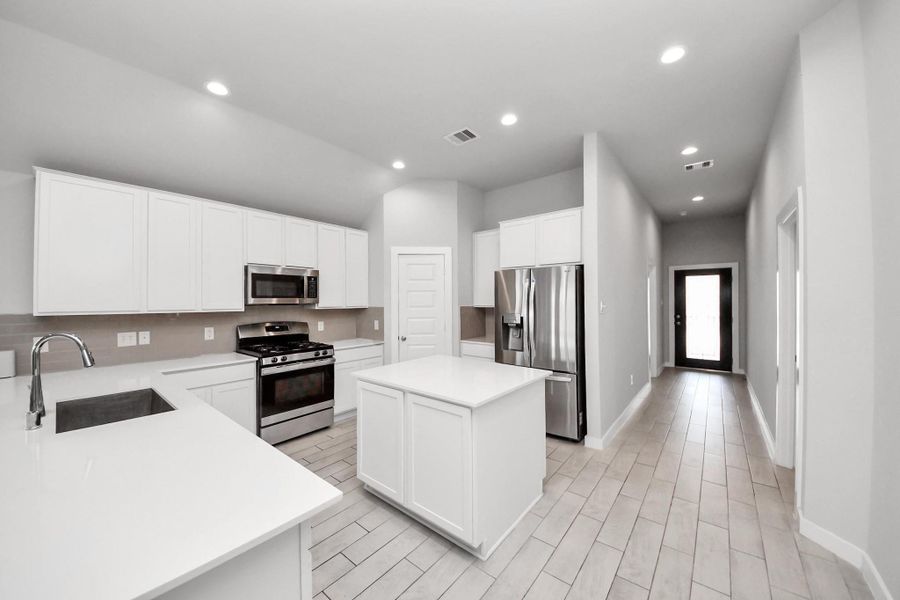 Bright and functional kitchen with generous counter space and a center island perfect for meal prep or gathering, with a view toward the entry hallway leading to the front door.